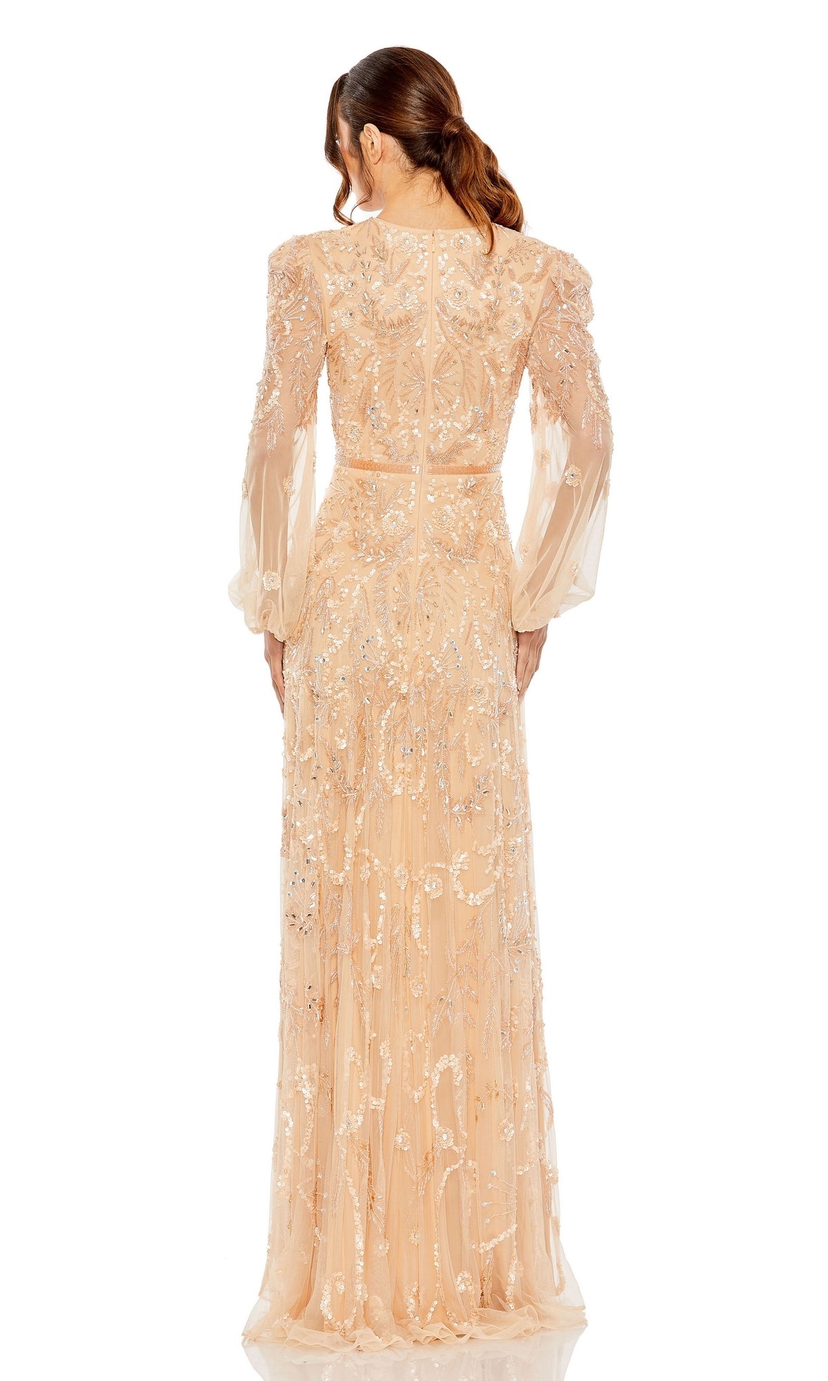 A woman with brown hair in a low ponytail models the Mac Duggal 93930 Long Sleeve Beaded Formal Gown, an elegant nude-colored dress with intricate beading and embroidery, seen from the back against a white background.